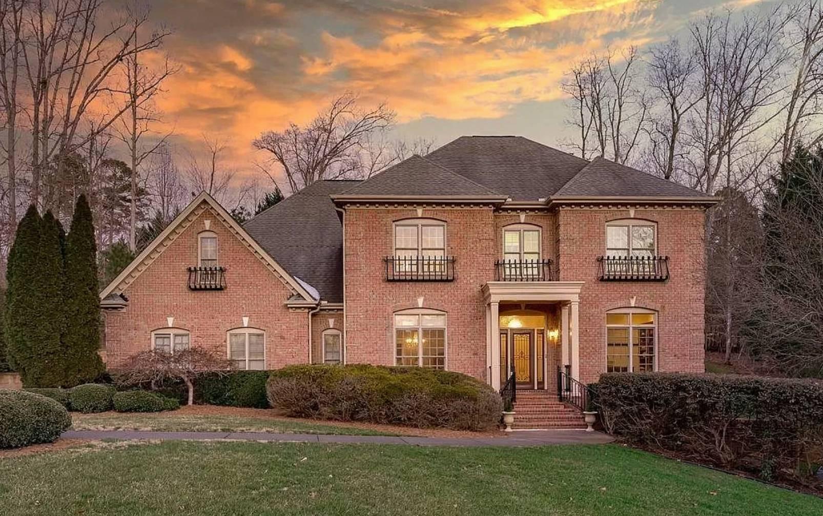 A stunning multistory red brick home with arched windows, cream trim, a gray roof, an impressive entryway, mature landscaping with shrubs and trees